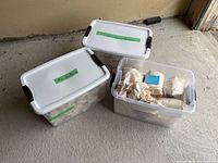 Three plastic Sterilite storage totes with white lids and black latches, some open showing wrapped ceramic items inside.
