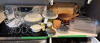 Wide shot of all kitchen items arranged on countertop including salad spinner, cutting boards, graters, garlic holder, casserole dish, wooden bowl and utensils, and wire rack.