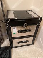 Front and side view showing mirrored panels, black faux leather trim with silver rivets, front latch, and two drawers with handles.
