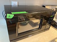 Black Master Chef microwave shown from the front angled view on a countertop with digital display lighted.