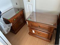 Two matching wood finish end tables with protective clear glass tops side by side