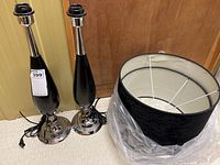 Pair of black and chrome table lamps and one black lampshade with packaging showing the lamps and shade together.