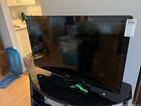 Front view of Phillips 40 inch flat-panel television on black curved glass stand with remote control taped on the stand.