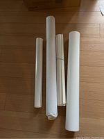 Four rolled posters placed on wooden floor, varying sizes and wrapped condition.