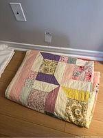 Quilt folded on wooden floor, showing multiple fabric squares in various colors and patterns