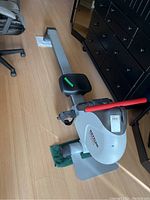 Full side angle view showing sliding seat on metal rail and flywheel housing with red handlebar and black foot straps