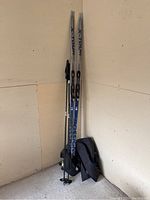 Full view showing two Rossignol X-Tour Venture skis, two ski poles, and a travel bag standing upright against wall.