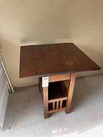 Front angle view of the wooden drop leaf table with magazine rack below.