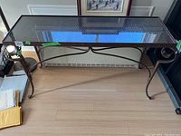 Full frontal view of metal sofa table showing glass top and frame details, including curled metal scroll legs.