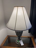 Full view of the table lamp showing the white fabric shade and the metal base on a glass surface.