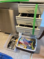 Photo shows three drawers of kitchen utensils and two baskets on the floor with various kitchen items.