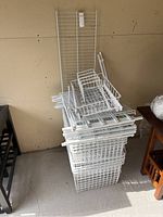 Full view of disassembled shelving rack components stacked together showing baskets, shelves, and frame parts in white metal wire construction.