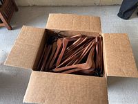 Top-down view showing large cardboard box filled with wooden hangers with metal hooks.