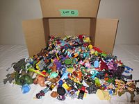 Wide view of entire box filled with assorted action figures piled together, showing many small and medium-sized plastic figures in various colors and styles.