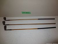Three antique golf clubs laid flat showing full length of shafts and club heads
