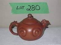 Front side view showing rounded pot with swirl designs and dragon head spout and handle, with lid on top