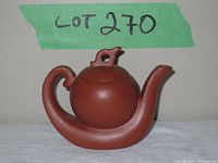Front and side view of the reddish clay teapot on white cloth with green label in background labeled Lot 270.
