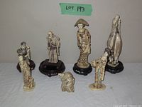 Front view of all seven figures on table, four on wood stands and three without