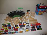 Photo showing all lot contents including multiple wooden toy trains, track pieces, and the wooden train roundhouse building.