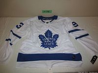 White hockey jersey laid flat showing front with Toronto Maple Leafs large blue maple leaf logo and number 93 on sleeves.