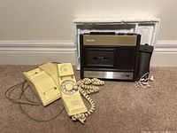 Philips cassette recorder and Northern Electric rotary phone together on floor with power charger and earphone