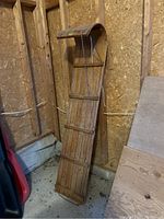 Full view of antique wooden toboggan leaning against wall, showing slatted wood construction and braided string.