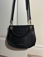 Front view of black Danielle Nicole crossbody purse with removable strap, hanging open, showing gold hardware and logo.