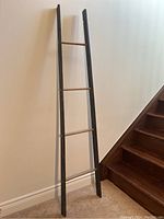 Full view of the rustic wooden ladder leaning against a white wall near wooden staircase showing overall height and design.