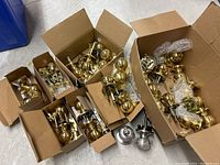 Multiple cardboard boxes containing approximately 30 doorknobs, mostly brass spherical style with mounting hardware and screws loosely arranged inside.
