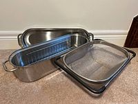 Side view of the stainless steel fish poacher and the expandable colander on the floor.