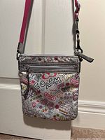 Front view of girls crossbody purse with colorful Coach graffiti print and front zipper pocket.