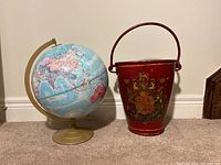Side view of textured globe on gold stand next to decorative red bucket with crest