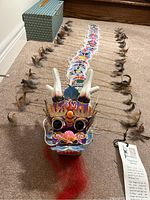 Photo of the full dragon kite laid out on floor with segmented bamboo body and feather accents, head attached and case visible.