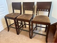 Front view of three matching hardwood stools with brown cushioned seats and circular cutouts on backrests.
