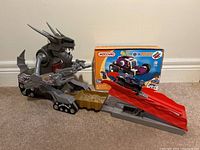 Wide view of Meccano dragon/mechanized monster figure on tracked platform with attached launcher and ramp, with box in background.