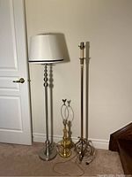 Three lamps side by side: silver floor lamp with white lampshade, brass floor lamp with wear, and brass butterfly table lamp.