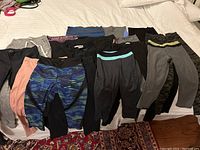 Lot of 16 assorted womens leggings and athletic pants laid out on a bed in various colors showing front and back views.