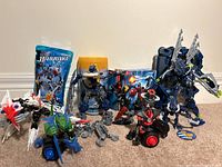 Photo showing multiple LEGO Bionicle figures arranged with boxes and instruction booklets in the back, featuring Barraki Pridak, Bordakh, Thulox, and others
