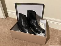 Photo of the boots inside an open shoebox showing the pair of black ankle boots with side zipper alongside white tissue paper.