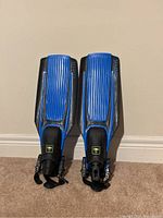 Front view of the pair of Stratos blue and black adjustable heel scuba fins against a beige wall.