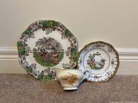 Set of two decorative china plates and one decorated ceramic pitcher arranged against a wall