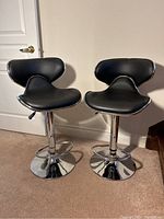 Front view of pair of black and chrome stools showing padded seats and backs with chrome trim.