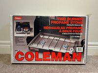 Front of box showing photo of stove, model number and branding in large red font. Details include pressure regulated, one year limited warranty, carry case image.