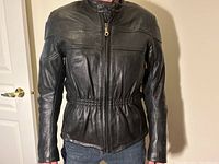 Front view of the black leather motorcycle jacket worn by a model showing elastic waist and zippered front.