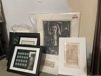 Several framed and matted print artworks stacked upright against the wall, showing portrait, abstract, and stylized designs.