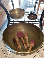 Three bowls displayed on shelving, large bowl on floor filled with mallets