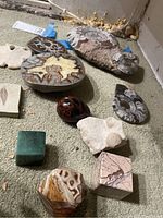 Ten-item assortment laid on carpet: multiple ammonite slices at rear, jasper egg, aventurine cube, marble cube, onyx dodecahedron and fossils front.