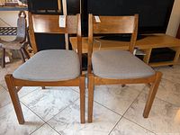 Front and side views of two wooden dining chairs with gray upholstered seats and rectangular backs.