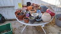 Overview of assortment of pots and planters on a white outdoor table showing various sizes and colors.