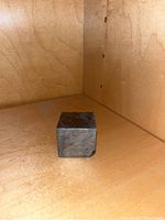 Front angled view of cube-shaped meteorite slice on plywood shelf